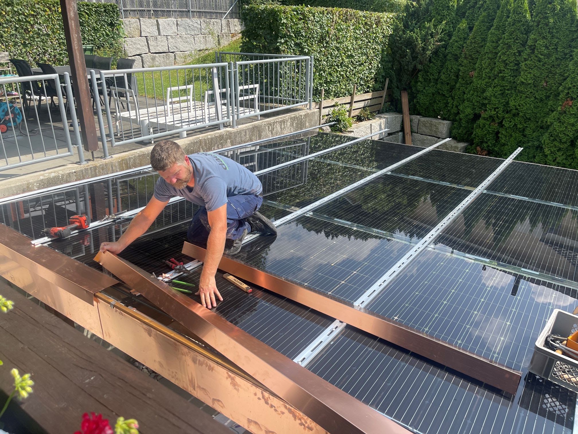 Monteur auf einer Pergola mit Solarmodulen und Kupferblech